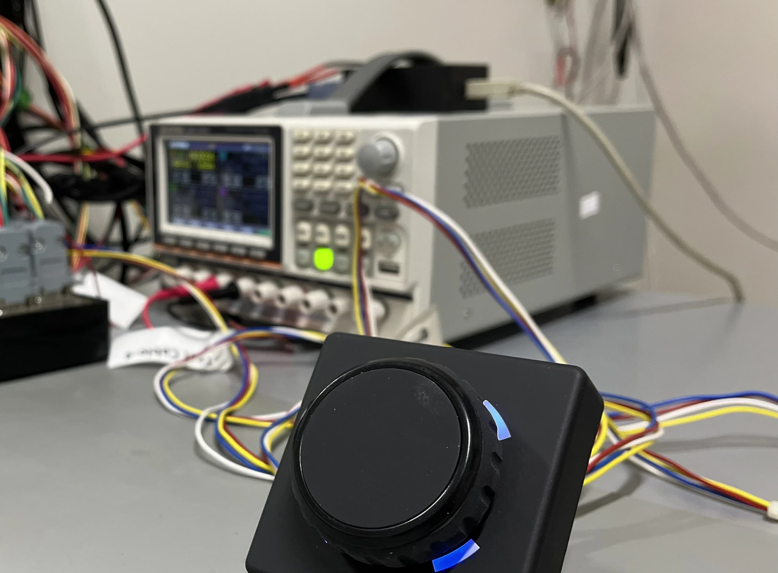 Rotary control unit wired to bench instruments during functional testing, its LED ring lit